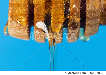 Dripping honey from a wooden spoon close-up macro. Blue background Dripping honey from a wooden spoon close-up macro. Blue background 86863033