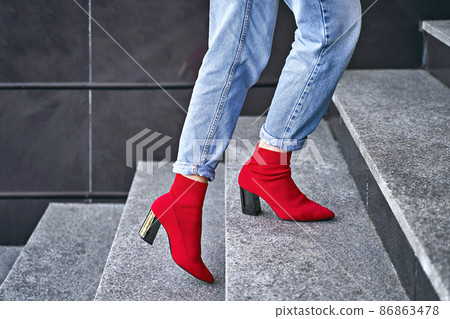 Woman legs in red sexy trendy stretch knitted fabric pointed toe block heel sock boots shoes and blue denim jeans pants 86863478