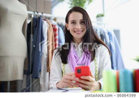 A woman seamstress holds a smartphone, close-up A woman seamstress holds a smartphone, close-up 86864399