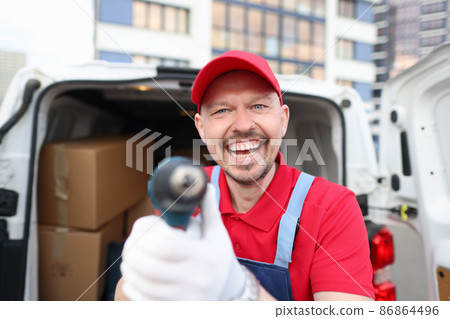 Happy courier in a red uniform shows a tool near a covered van Happy courier in a red uniform shows a tool near a covered van 86864496