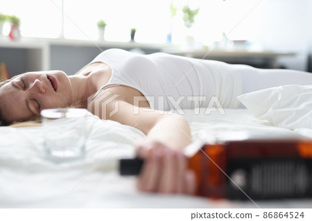 Drunk woman sleeps alone on a bed with a bottle 86864524