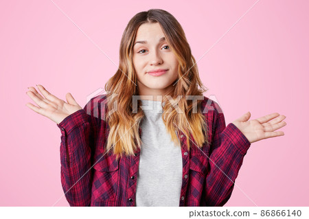 Pretty young woman throws up hands, shows her uncertainty and doubt, dressed in casual checkered shirt, isolated over pink background. Indecisive young female shrugs shoulders in bewilderment Pretty young woman throws up hands, shows her uncertainty and doubt, dressed in casual checkered shirt, isolated over pink background. Indecisive young female shrugs shoulders in bewilderment 86866140