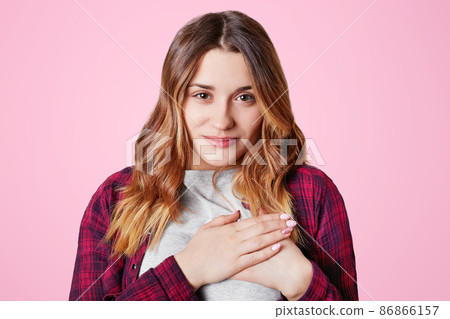 Body language concept. Gorgeous friendly looking young female in casual t shirt, keeps hands on chest, expresses her gratitude and gratefulness, says thanks, isolated over pink background. Body language concept. Gorgeous friendly looking young female in casual t shirt, keeps hands on chest, expresses her gratitude and gratefulness, says thanks, isolated over pink background. 86866157