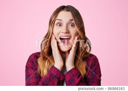 Photo of excited pretty woman looks in amazement, bugged eyes and widely opened eyes, being pleasantly shocked to recieve present, isolated over pink backgroud. Emotional female poses indoor Photo of excited pretty woman looks in amazement, bugged eyes and widely opened eyes, being pleasantly shocked to recieve present, isolated over pink backgroud. Emotional female poses indoor 86866161
