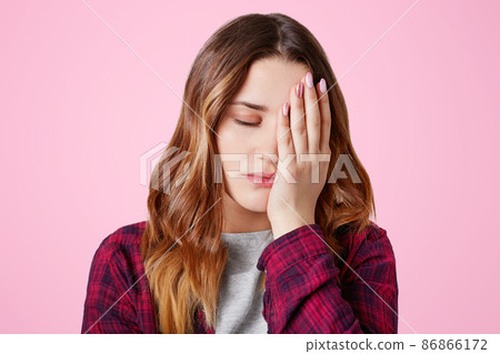 Fatigue good looking young woman has sleepy expression, covers eyes with hand, being overworked, prepared course or diploma paper all night, isolated over pink background. Tiredness and work concept Fatigue good looking young woman has sleepy expression, covers eyes with hand, being overworked, prepared course or diploma paper all night, isolated over pink background. Tiredness and work concept 86866172