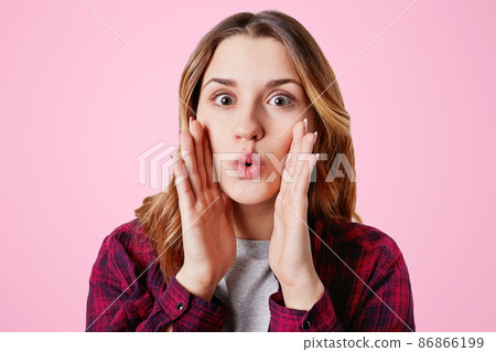 Amazed pretty lovely woman rounds lips as says wow, keeps hands on cheeks, being shocked, gestures in studio, isolated over pink background. Attractive young female model gossips with friends Amazed pretty lovely woman rounds lips as says wow, keeps hands on cheeks, being shocked, gestures in studio, isolated over pink background. Attractive young female model gossips with friends 86866199
