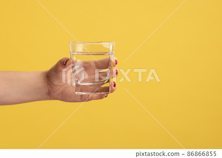 Close up woman hand holding glass with water, advertising of fresh pure beverage, best way to restore water balance. Indoor studio shot isolated on yellow background. Close up woman hand holding glass with water, advertising of fresh pure beverage, best way to restore water balance. Indoor studio shot isolated on yellow background. 86866855