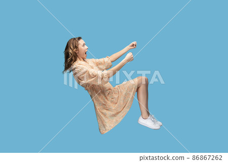 Hovering in air. Amazed girl levitating in driving seat position, holding invisible steering wheel, looking shocked, open mouth surprised by high speed, watching unbelievable. studio shot isolated Hovering in air. Amazed girl levitating in driving seat position, holding invisible steering wheel, looking shocked, open mouth surprised by high speed, watching unbelievable. studio shot isolated 86867262