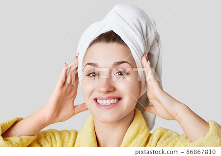 Close up shot of glad satisfied woman being happy after spa procedure, has fresh soft healthy skin, broad smile, white perfect teeth, wears white towel on head, isolated over white background Close up shot of glad satisfied woman being happy after spa procedure, has fresh soft healthy skin, broad smile, white perfect teeth, wears white towel on head, isolated over white background 86867810