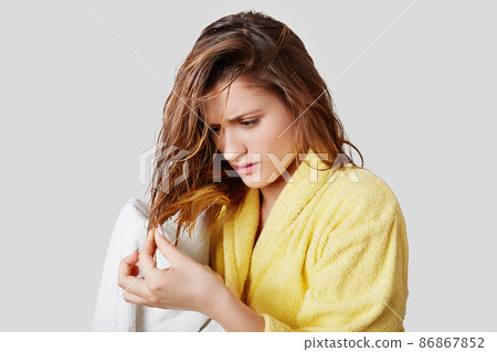 Pretty woman looks desprately at split ends of hair after taking shower, being discontent with water or shampoo which spoils her hair, tries to solve problem, isolated over white background. Pretty woman looks desprately at split ends of hair after taking shower, being discontent with water or shampoo which spoils her hair, tries to solve problem, isolated over white background. 86867852