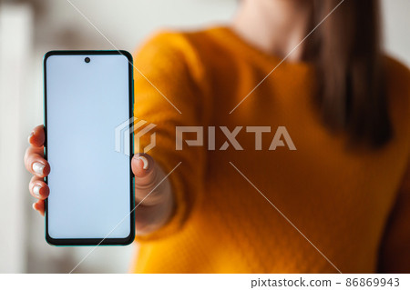 Woman hold mobile phone screen mockup in hands in orange sweater 86869943