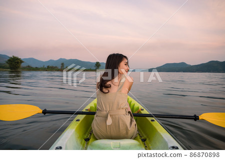 Beautiful young asian woman holding paddle in canoe on lake at evening on vacation 86870898