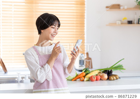 A young woman operating a smartphone in the kitchen A young woman operating a smartphone in the kitchen 86871229