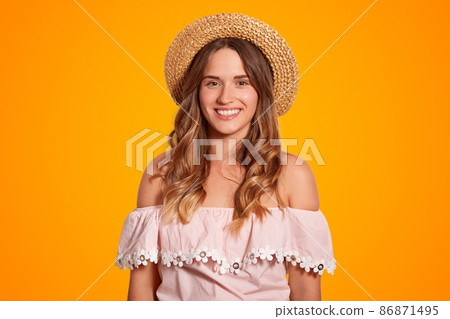 Waist up portrait of delighted beautiful young female traveller with broad smile, healthy pure skin, dressed in summer hat and blouse, poses in studio, rejoices summer vacations. Recreation concept 86871495