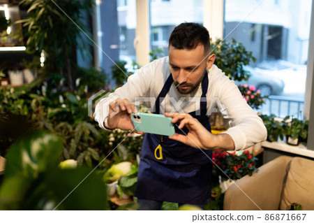 businessman botanist in the garden center photographing flowers on a smartphone businessman botanist in the garden center photographing flowers on a smartphone 86871667