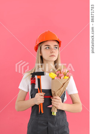 Builder woman with bouquet and hammer on pink background Builder woman with bouquet and hammer on pink background 86871783
