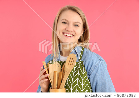 Housewife with wooden kitchen utensils on pink background Housewife with wooden kitchen utensils on pink background 86872088