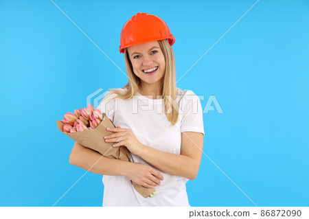Builder girl with bouquet of flowers on blue background 86872090