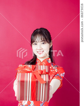 Portrait of a young asian woman wearing traditional cheongsam qipao dress holding gift isolated over red background. Portrait of a young asian woman wearing traditional cheongsam qipao dress holding gift isolated over red background. 86873016
