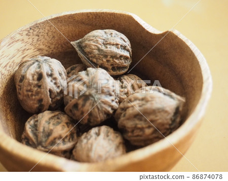 Walnuts with shells in a wooden bowl Walnuts with shells in a wooden bowl 86874078