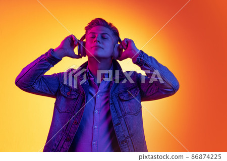 Half-length portrait of young handsome man in casual youth style clothes isolated on orange background in neon light, filter. Concept of emotions, beauty, fashion 86874225
