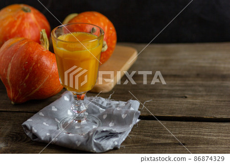 Pumpkin smoothie, spicy latte in a glass. In the background in blur orange pumpkins on a wooden vintage background. Copy space. Cozy table in hygge style 86874329