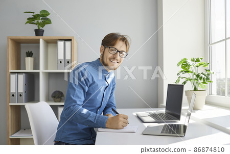 Portrait of smiling millennial Caucasian male freelancer work on laptops at home office. Happy young businessman use computers consult client. Guy studying on web on gadgets. Technology concept. 86874810
