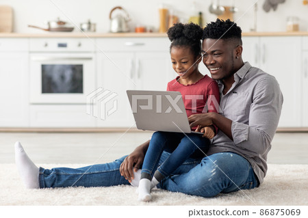 Happy black father and daughter using notebook together at home Happy black father and daughter using notebook together at home 86875069