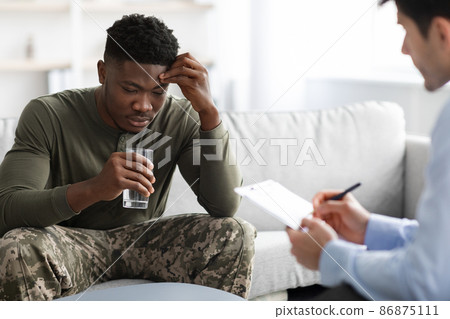 Emotional black military man drinking water while talking to psychotherapist 86875111
