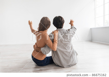 Happy young caucasian guy and woman planning future home interior sit on floor in white empty room interior Happy young caucasian guy and woman planning future home interior sit on floor in white empty room interior 86875162