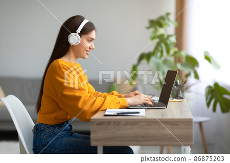 Young Caucasian lady in headphones using laptop pc, working online from home, copy space 86875203