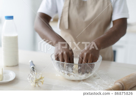 Cropped millennial african american woman in apron making dough on table in kitchen interior, close up Cropped millennial african american woman in apron making dough on table in kitchen interior, close up 86875826