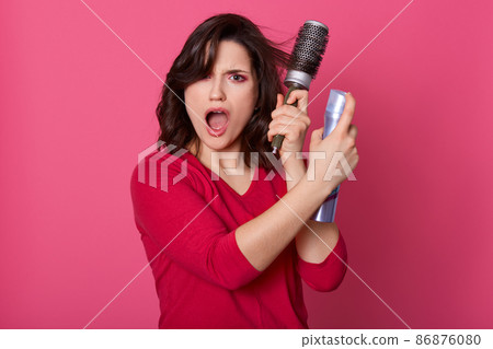 Close up portrait of young displeased emotional woman having indignation, opening eyes and mouth widely, looking directly at camera, dealing with hair with help of hairbrush and liquid for fixation. Close up portrait of young displeased emotional woman having indignation, opening eyes and mouth widely, looking directly at camera, dealing with hair with help of hairbrush and liquid for fixation. 86876080