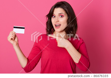 Picture of emotional good looking pretty female pointing with forefinger at credit card, having surprised facial expression, opening mouth, doing shopping online. Women and purchases concept. 86876103