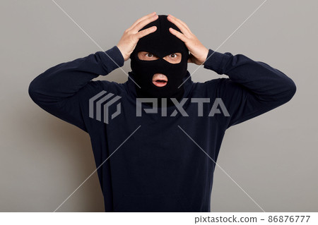 Shocked and frightened criminal, thief catching on place of committing crime, looking at camera with frightened eyes, holding his head, does not understand what to do, isolated over gray background. 86876777