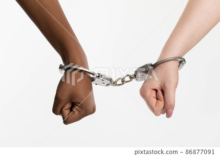 A clenched fist. Two female hands handcuffed. Two human races connected by steel handcuffs. Arrest of the guilty. 86877091