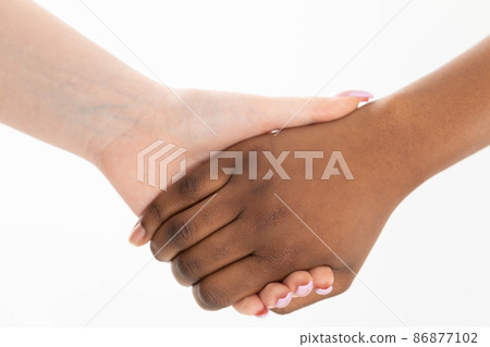 Two hands in a cordial embrace. Handshake. Two women holding hands. Two hands of different races in a loving embrace. African and European. Two hands in a cordial embrace. Handshake. Two women holding hands. Two hands of different races in a loving embrace. African and European. 86877102
