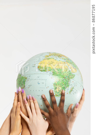 Four young adult girls hold the globe above their heads and gently embrace it with their hands. Colored hands of different races. 86877195