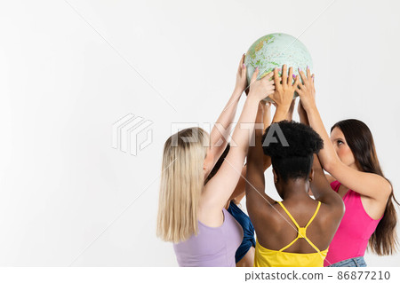 Four young adult girls hold the globe above their heads and gently embrace it with their hands. Colored hands of different races. 86877210
