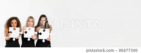 A panoramic shot of three teenagers of different races holding puzzle pieces in their hands stretched far in front of them. Racial tolerance. 86877300