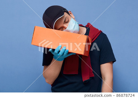 Indoor shot of tired online shop employee or delivery man sleeping while holding carton box with clients order, works overtime during quarantine, being exhausted, put head on parcel and slumbering. Indoor shot of tired online shop employee or delivery man sleeping while holding carton box with clients order, works overtime during quarantine, being exhausted, put head on parcel and slumbering. 86878724