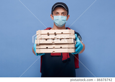 Closeup portrait of young guy handing pizza's boxes to customer, delivery man wearing protective mask and latex gloves, trying to avoid infection of coronavirus. Covid 19, quarantine concept. 86878742