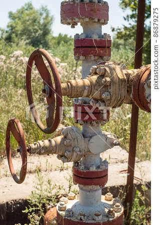 Old abandoned pipes and valves from an oil rig left over from oil production. Rust and peeling paint on the pipes. Pollution of the environment 86879275