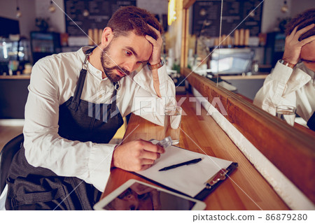 Tired male barista with pills sitting at wooden counter in cafe 86879280