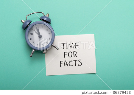 on a blue background lies an alarm clock with a note time for facts 86879438