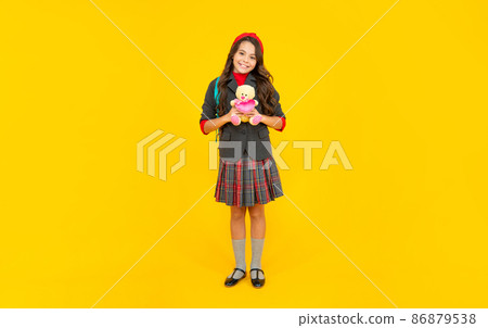 happy teen girl in uniform with school bag holding toy on yellow background, education happy teen girl in uniform with school bag holding toy on yellow background, education 86879538