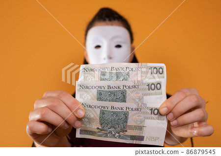 An anonymous woman stands and pulls her hand in with paper banknotes with the face value of one hundred Polish zlotys. No face because there's a mask on it. An anonymous woman stands and pulls her hand in with paper banknotes with the face value of one hundred Polish zlotys. No face because there's a mask on it. 86879545