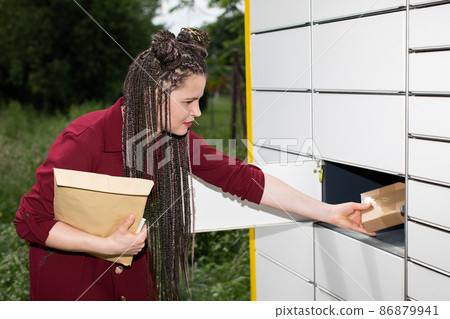 A teenager takes a parcel out of a parcel locker. Open mailbox. The girl pulls all the parcels from the letterbox. 86879941