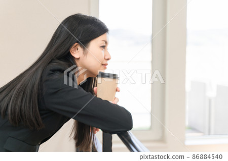 A business woman relaxing with her elbows on the railing and a coffee cup A business woman relaxing with her elbows on the railing and a coffee cup 86884540