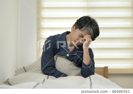 A man in his 50s sitting in bed and holding his head 86886561